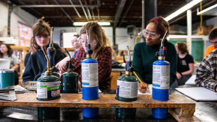 three students at a lab table, working with chemicals and taking notes