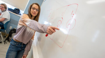 Teaching Assistant working out physics problem on whiteboard