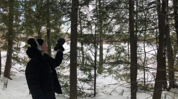 Jillian Trujillo, outside in winter, holding up a microphone to capture nature sounds