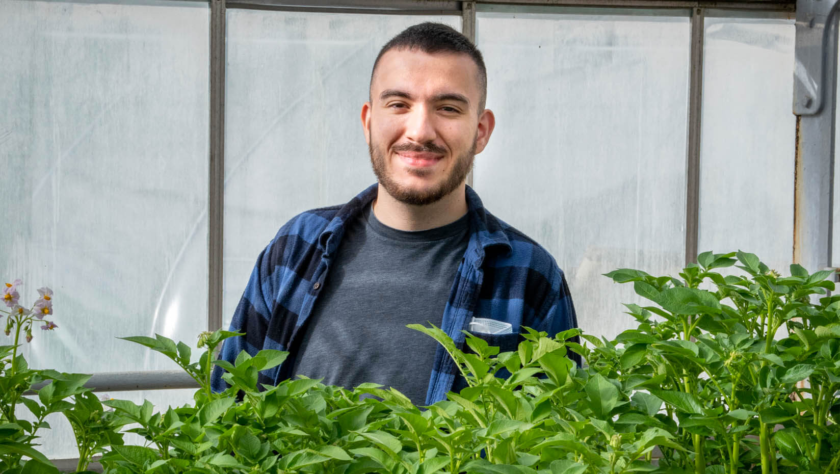 Ross Sousa posing with plants in a greenhouse