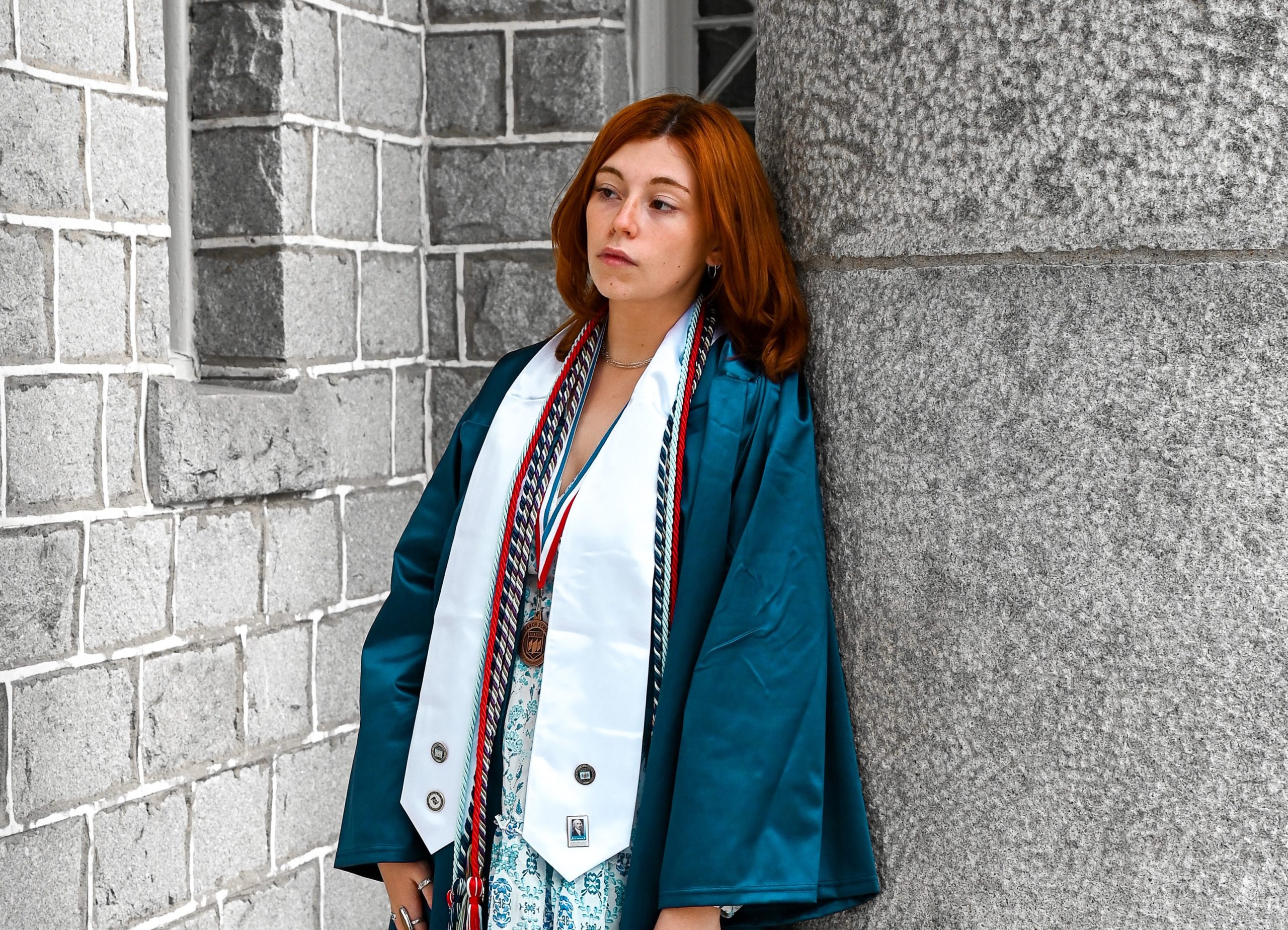 Laura Curioli, in UMaine graduation regalia, leaning against the pillar of a campus building.