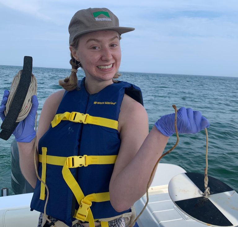 Jamie Fogg, posing for the camera while standing in a boat, holding testing equipment.