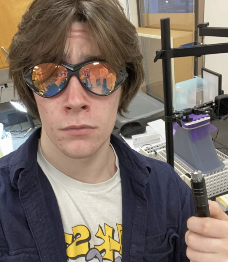 Richard Viveiros poses for the camera wearing his sunglasses and holding up a piece of lab equipment
