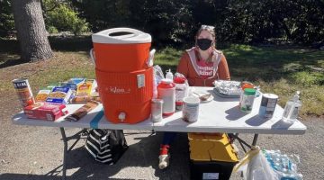 Brenna Jones sits behind a table bearing food and drinks for the unhoused and precariously housed.