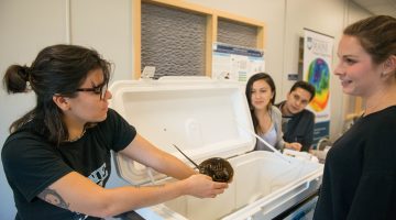 A graduate student holds out a horseshoe crab for inspection by another student during the Grad School Open House