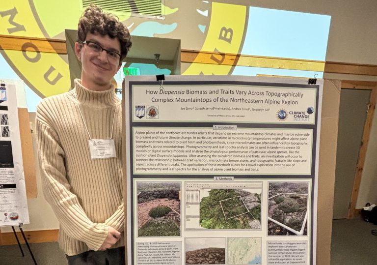 Joe Zeno poses beside a a poster featuring his work on alpine plants