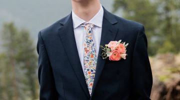 Josh Adell, wearing a dark suit and pink boutonniere, poses for a photo outside.